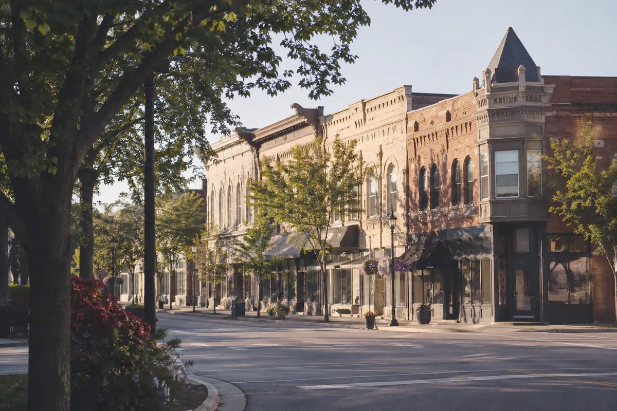 Illustration of Plymouth: historic brick storefronts along a leafy downtown street.