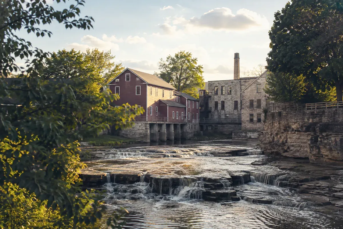 Illustration of Sheboygan Falls: river cascades below old mill buildings and trees.